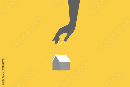 Close up of hand putting coin in house piggy bank.
