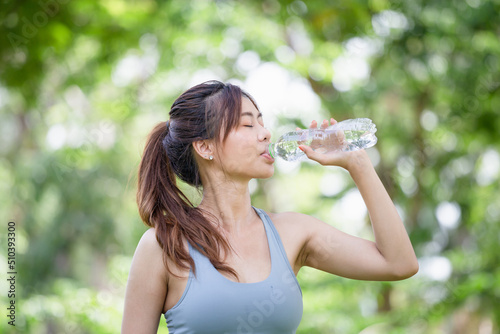 Athlete young beautiful woman drinking water from a plastic bottle at summer green park, Sport woman drinking water after work out exercising