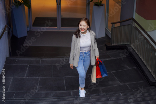 Smiling Asian woman with shopping bags above the floor of a department store in a shopping mall facility. Women's fashion, shopping, lifestyle, happiness, consumption, sales and people concept.