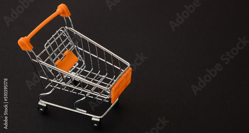 Mini orange supermarket trolley on black background. Shopping concept