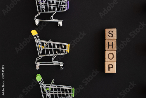 Mini color supermarket trolleys and word shop on black background. Shopping concept
