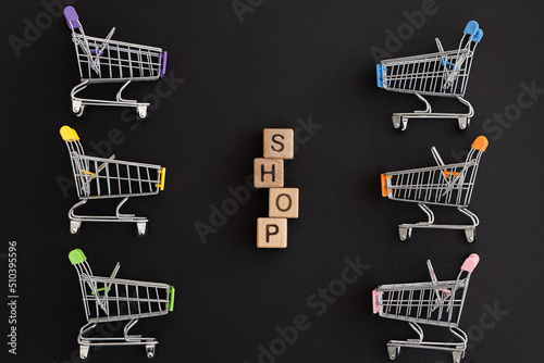 Mini color supermarket trolleys and word shop on black background. Shopping concept