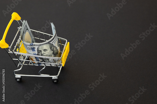 Small shopping cart with 100 dollar banknote on black background