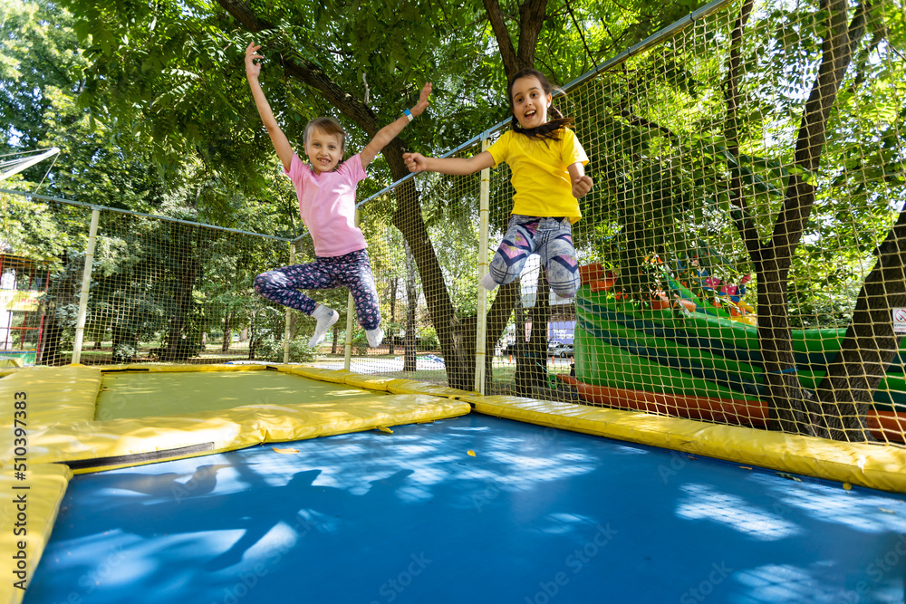 Two little girls in the summer jump on a trampoline, smiling and ...