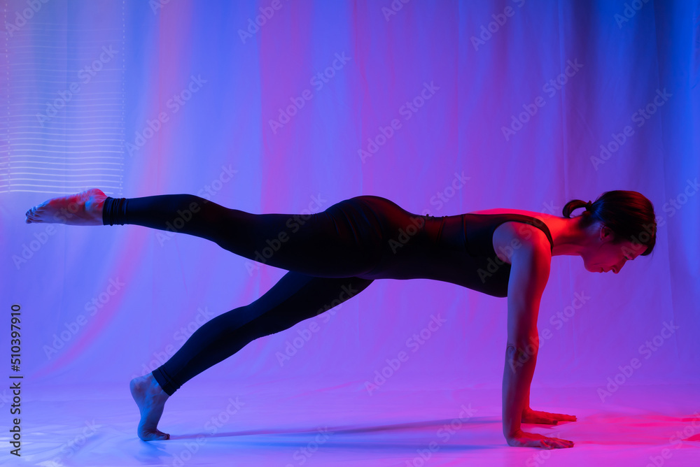 Athletic woman in high school, swimsuit and leggings, doing yoga, push-ups or push-ups, falancasana, plank pose variation, beautiful girl exercising at home or in a yoga studio