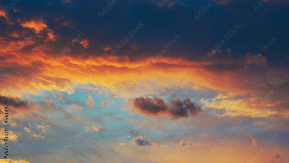 Cloudy sky at sunset. Dark blue and yellow natural background or wallpaper. The rays of the setting sun effectively illuminate the clouds. Beautiful and spectacular setting sky. Nightfall cloudscape