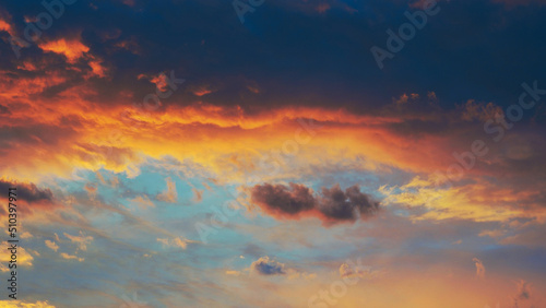 Cloudy sky at sunset. Dark blue and yellow natural background or wallpaper. The rays of the setting sun effectively illuminate the clouds. Beautiful and spectacular setting sky. Nightfall cloudscape