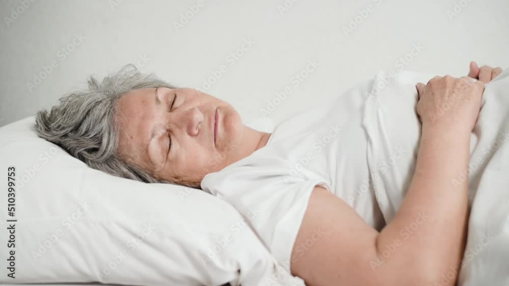 Sleeping senior woman has nightmare. Side view of an excited older woman tossing and turning on bed in bedroom. Elderly people and mental health concept. Sleeping senior woman has nightmare. Side view of an excited older woman tossing and turning on bed in bedroom. Elderly people and mental health concept.