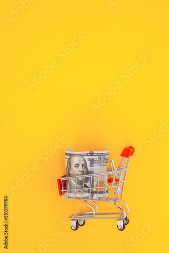 Shopping cart with dollar banknotes on a yellow background.Business finance shopping concept.Saving currency. Investments. Copy space
