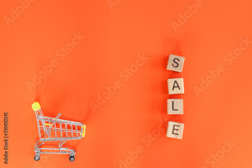 Small metal cart and word sale on red background. Shopping concept