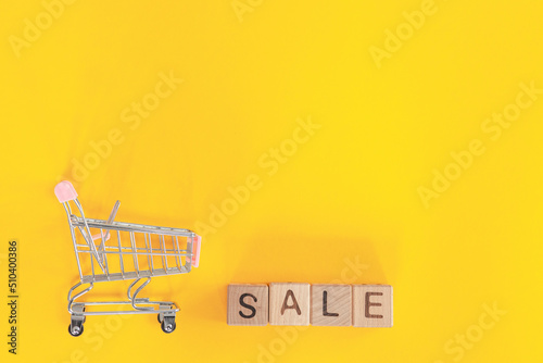 Small metal cart and word sale on yellow background. Shopping concept