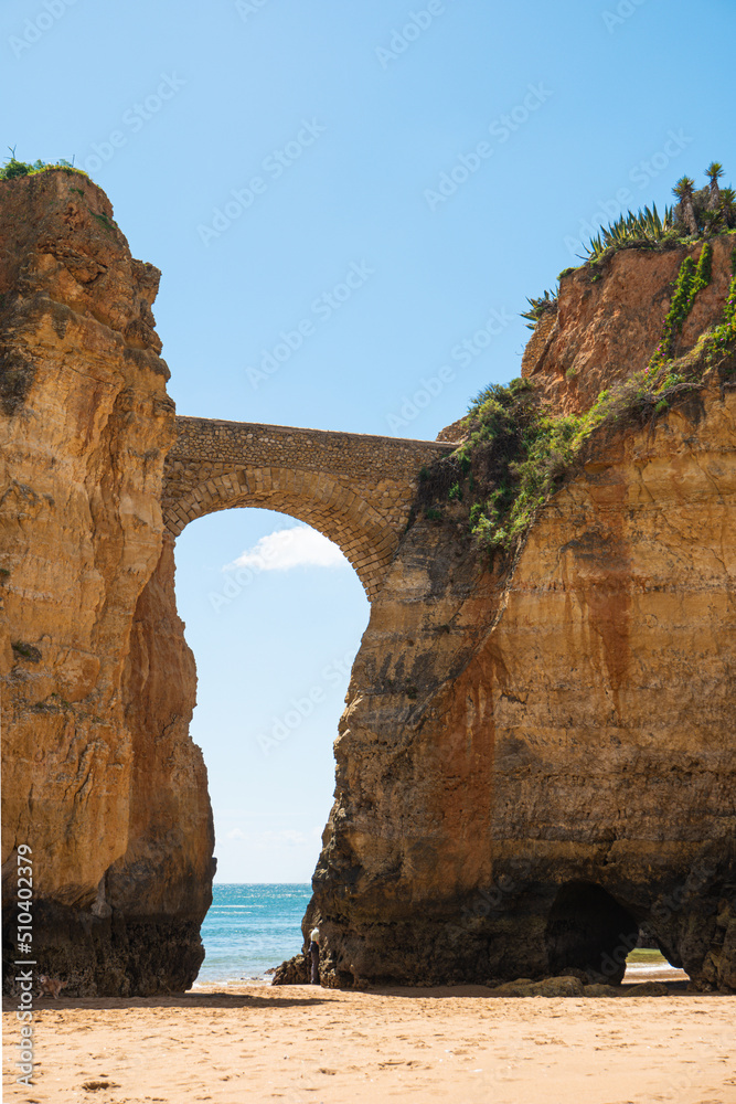Surrounded by cliffs picturesque Praia dos Estudantes or sandy Beach of Students in Lagos, Algarve. Beautiful arch link one of the rocks with the mainland landscape during cloudy weather. Portugal