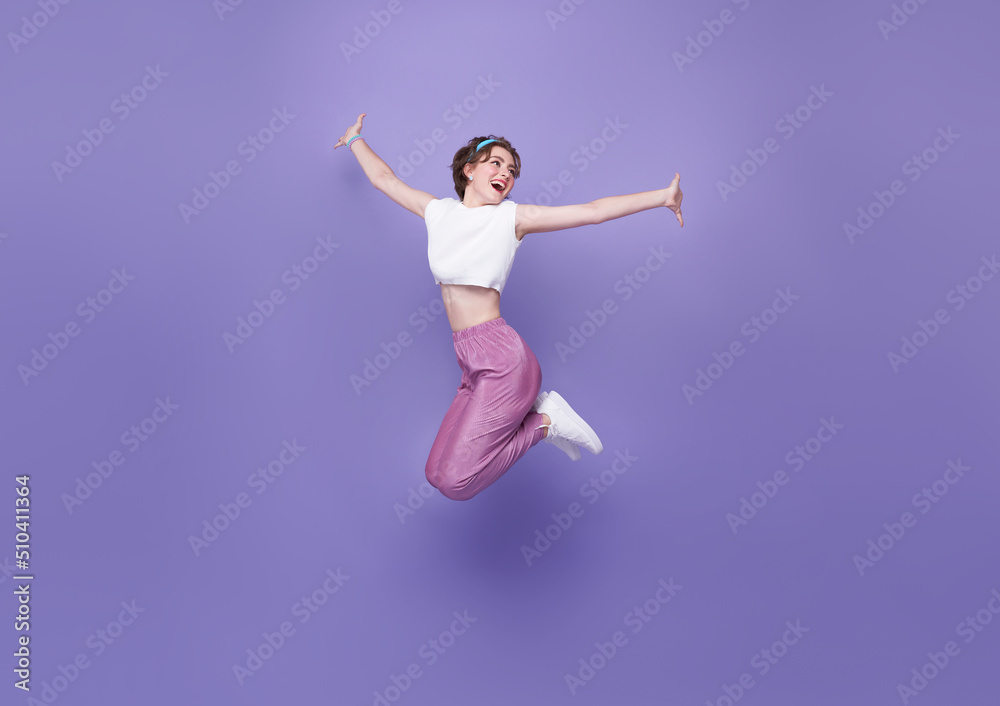Happy woman smiling and jumping while celebrating success isolated on violet background.