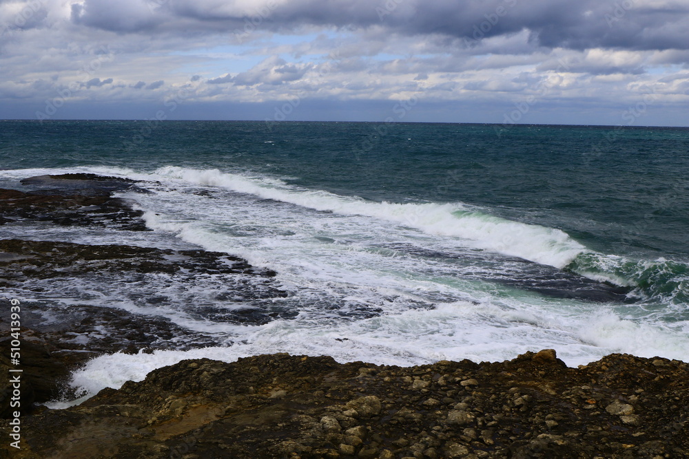 Smooth waves on sea reaching to rocky shore.