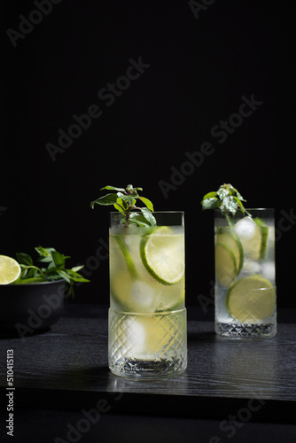 Dos vasos de refrescante zumo de lima con rodajas de lima y hielo sobre fondo negro photo