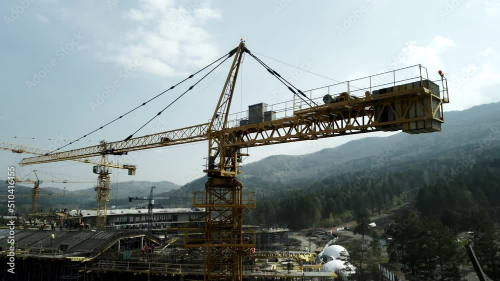 Construction in mountainous areas. Many construction cranes operate during the daytime. Flying around the yellow faucet. The blue sky together is a high mountain covered with green trees.