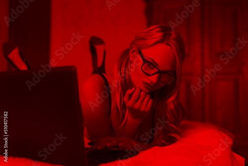 Sexy blonde woman typing on laptop in red light
