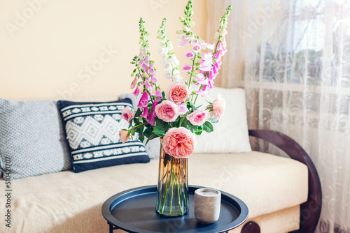 Fresh bouquet of roses and foxgloves flowers put in vase in living room. Interior and home decor. Pink orange blooms