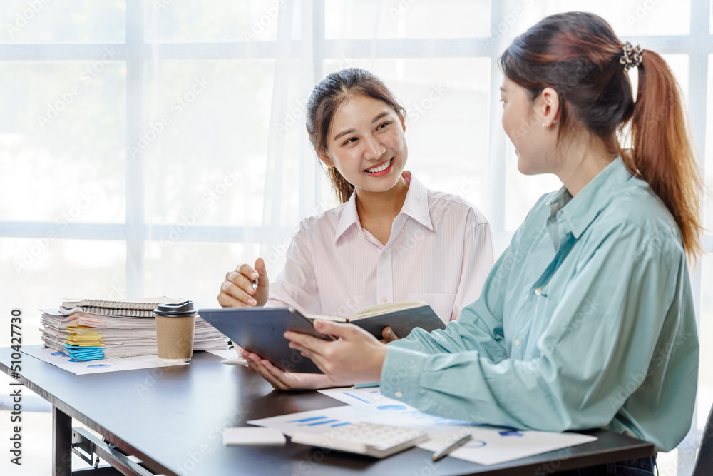 Two young asian woman using digital tablet while sitting in office workplace.