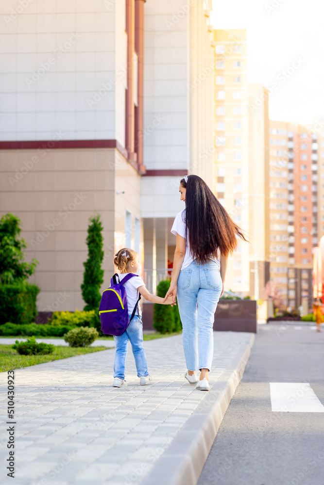 the first day of school, a parent leads a girl to a schoolgirl with a backpack by the hand to the first class, and back to school the first day of school, a parent leads a girl to a schoolgirl with a backpack by the hand to the first class, and back to school