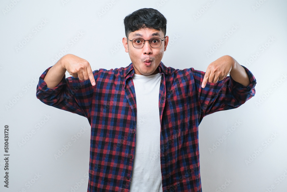 Naklejka premium Young handsome man pointing down with fingers showing advertisement, surprised face and open mouth