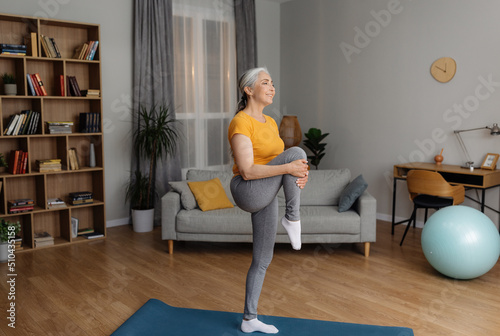 Domestic fitness. Fit senior woman in sportswear doing exercises on yoga mat, stretching her leg on home workout