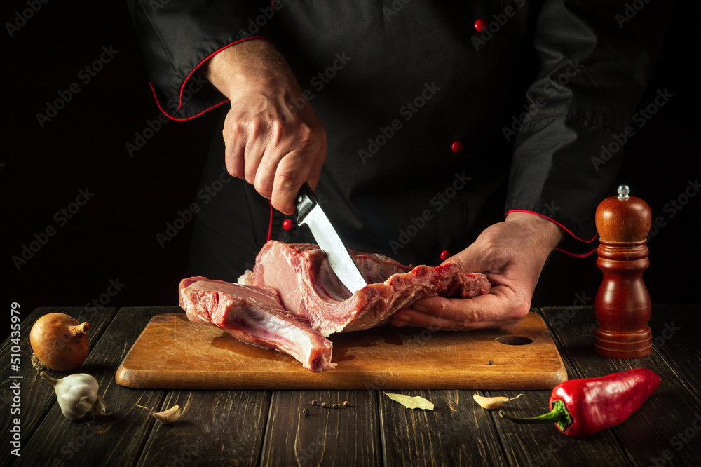 The chef cuts raw meat. Butcher cutting pork ribs. Meat with bone on a wooden cutting board. National cuisine.
