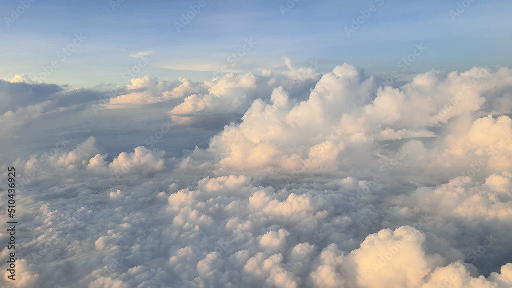 View from the window of the plane. The sky with white clouds and blue background. Clear weather with a light of sunlight sinking