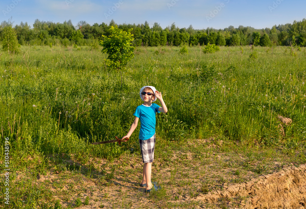 A 6-year-old boy in sunglasses and a white panama hat looks at the sky in surprise. In his hand is a toy sword. A 6-year-old boy in sunglasses and a white panama hat looks at the sky in surprise. In his hand is a toy sword.