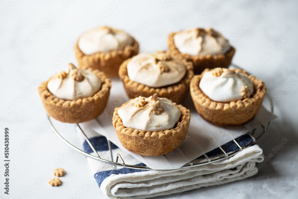 Lemon curd tartlets with whipped meringue on a wire rack on a gray background. Lemon curd tartlets with whipped meringue on a wire rack on a gray background.