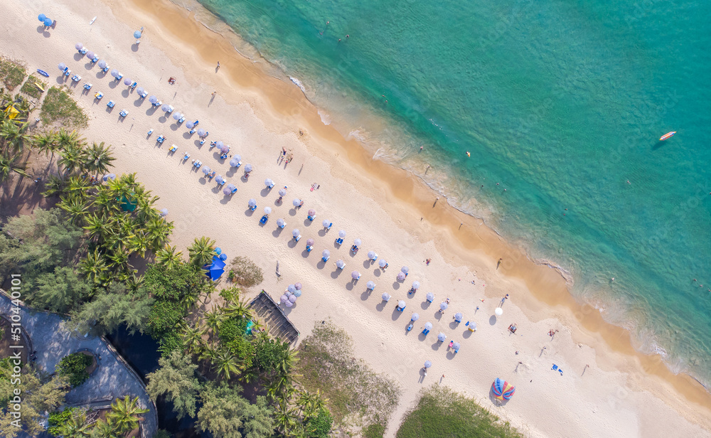 Aerial view of a white beach full of colored beach umbrellas and relaxed people swimming on a clear sea