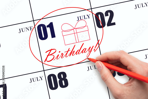 The hand circles the date on the calendar 1July, draws a gift box and writes the text Birthday. Holiday. photo