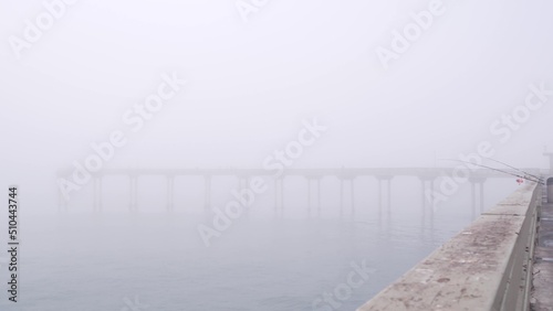 Wooden Ocean Beach pier in fog  misty California coast  USA. Foggy moody cloudy weather on San Diego shore. Calm tranquil silent atmosphere. Waterfront boardwalk. Fishing or recreational angling rod.