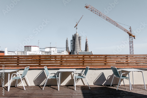 Tables and chairs on a terrace. In the background you can see cranes working and the towers of the Basilica of the Sagrada Familia in Barcelona under construction. photo