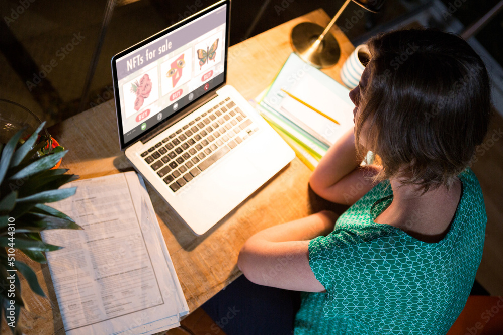 Caucasian businesswoman researching for non fungible tokens on laptop while working late in office Caucasian businesswoman researching for non fungible tokens on laptop while working late in office