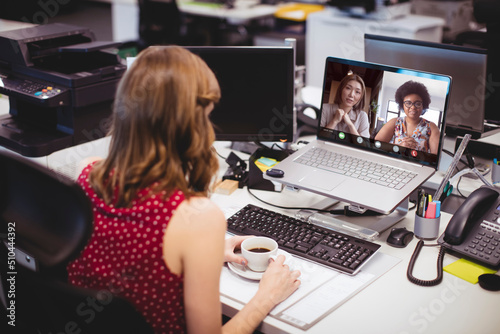 Caucasian female professional holding coffee cup video conferencing with colleagues over laptop