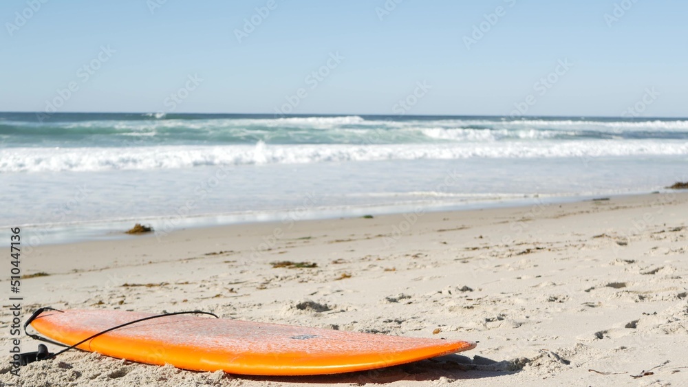 Surfboard for surfing lying on beach sand, California coast, USA. Ocean  waves and orange surf board