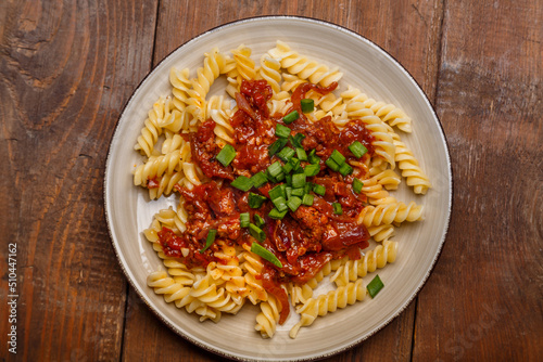 Plate with bolognese pasta on a wooden table sprinkled with green onions.