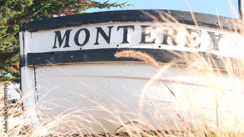 Monterey sign on white wooden boat stern, fisherman nautical vessel stem, bow or rostrum near Cannery Row and Bay Aquarium. Coniferous pine cypress tree. Historic capital, tourist city, California USA photo