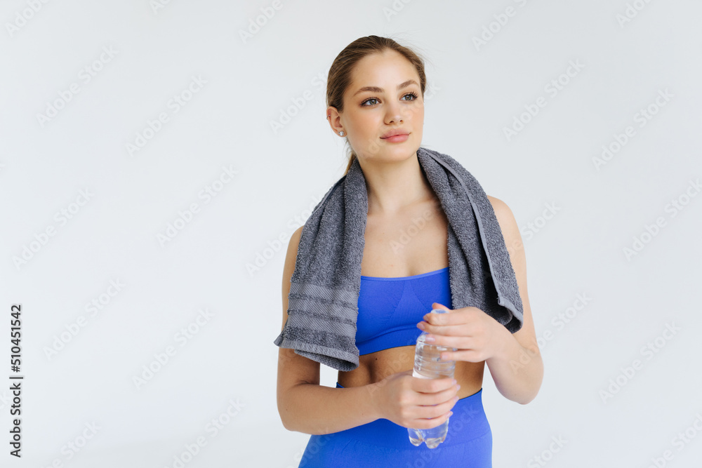 Young sportswoman with towel on shoulders holding sports bottle and looking at camera isolated on white background Young sportswoman with towel on shoulders holding sports bottle and looking at camera isolated on white background