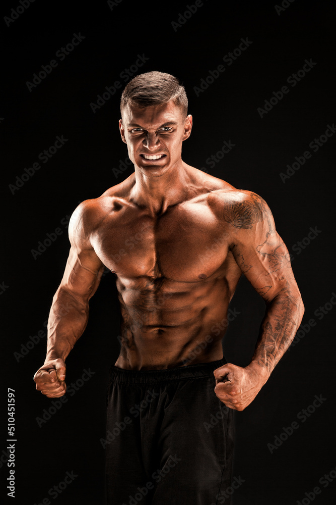 Fototapeta premium Handsome power athletic man confidently looking forward. Strong bodybuilder with six pack, perfect abs, shoulders, biceps, triceps and chest Isolated on black background