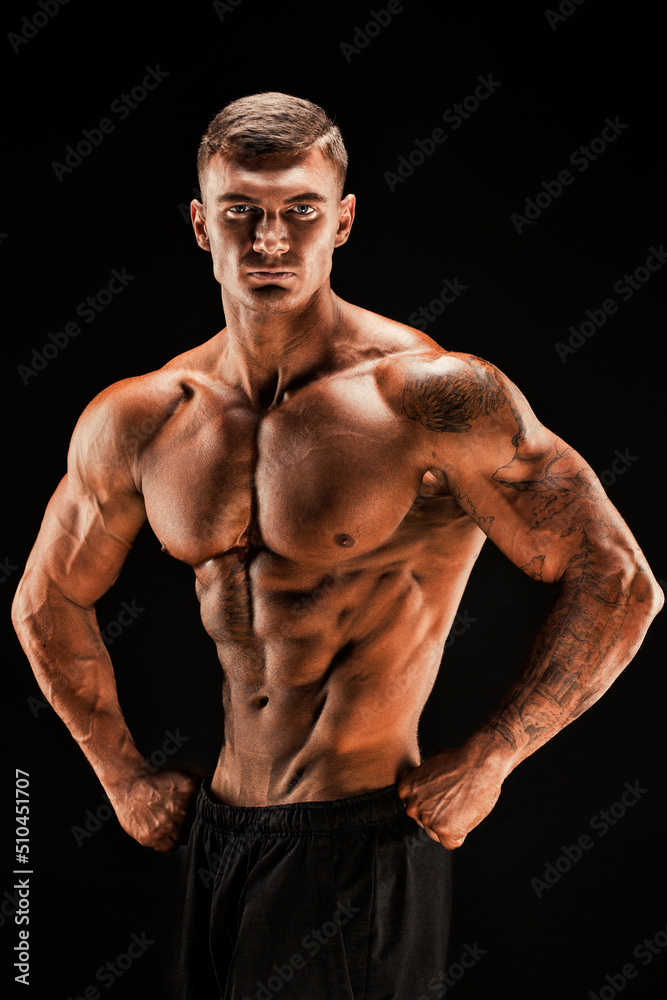 Handsome power athletic man confidently looking forward. Strong bodybuilder with six pack, perfect abs, shoulders, biceps, triceps and chest Isolated on black background Handsome power athletic man confidently looking forward. Strong bodybuilder with six pack, perfect abs, shoulders, biceps, triceps and chest Isolated on black background