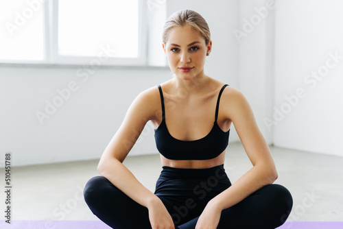 Relaxing after training. Beautiful young woman looking away while sitting on exercise mat at gym