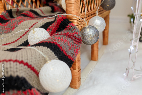 silver and white bulbs, baubles with knit scarf on wicker wurniture, closeup. Christmas decorated interior details