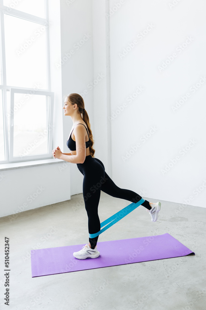 Fitness woman doing exercise for glutes with resistance band at home. Athletic girl working out