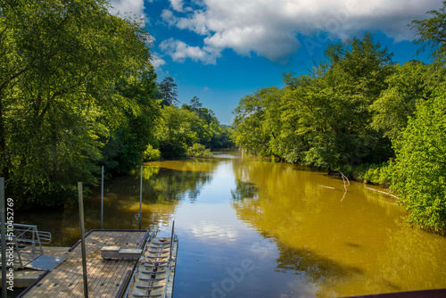 a gorgeous summer landscape in the park with the silky brown waters of Little River surrounded by lush green trees, grass and plants with blue sky and clouds at Olde Rope Mill Park in Woodstock photo