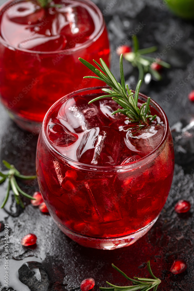 Pomegranate gin cocktail with lime, rosemary and ice on rustic black table Pomegranate gin cocktail with lime, rosemary and ice on rustic black table