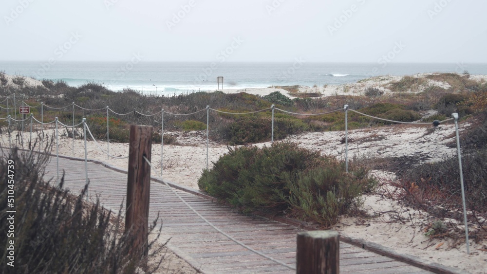 Ocean beach sandy dunes, Monterey nature, California misty coast, USA. Foggy rainy calm autumn or winter weather, grey cloudy sky. Trail path on shore near cold sea waves. Boardwalk from wooden planks Ocean beach sandy dunes, Monterey nature, California misty coast, USA. Foggy rainy calm autumn or winter weather, grey cloudy sky. Trail path on shore near cold sea waves. Boardwalk from wooden planks
