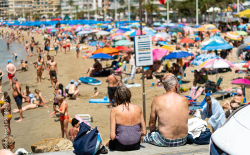Rear view of mature man and woman sitting, facing the beach full of people out of focus. photo