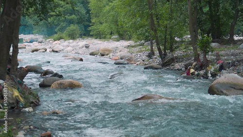 Slow motion shot of the Beas River flowing in between trees at Manali in Himachal Pradesh, India. View of the Beas river during the summer. Natural river in the forest background. photo